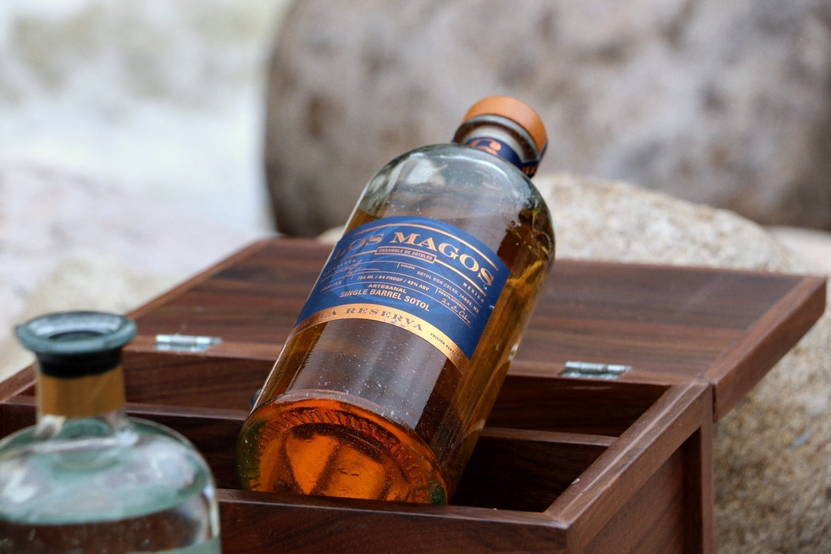 Bottle of Los Magos 6 Year Reserva sotol resting in a wooden presentation box on stone, Chihuahua