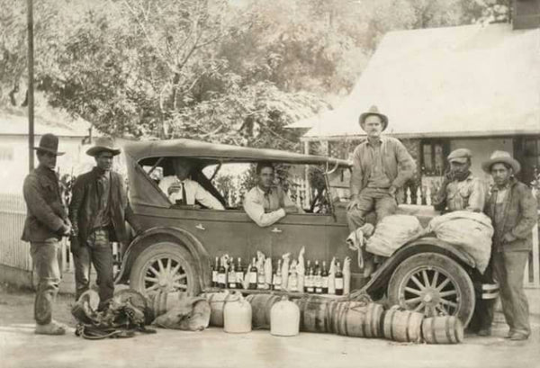 Vintage black and white photograph of men with an early automobile and barrels outside a rural building