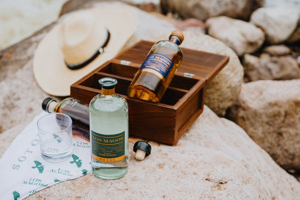 Los Magos 6 Year Reserva in a wooden box beside a bottle of Blanco and a cowboy hat on a rock